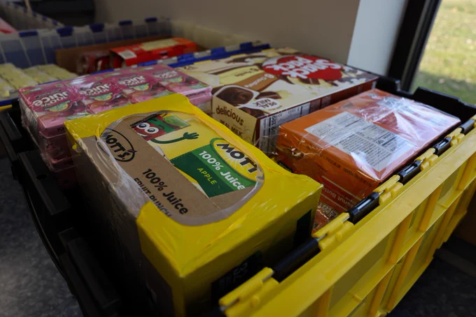 This image shows an array of food items inside plastic containers. There are packages of juice boxes and pudding cups in these containers. 