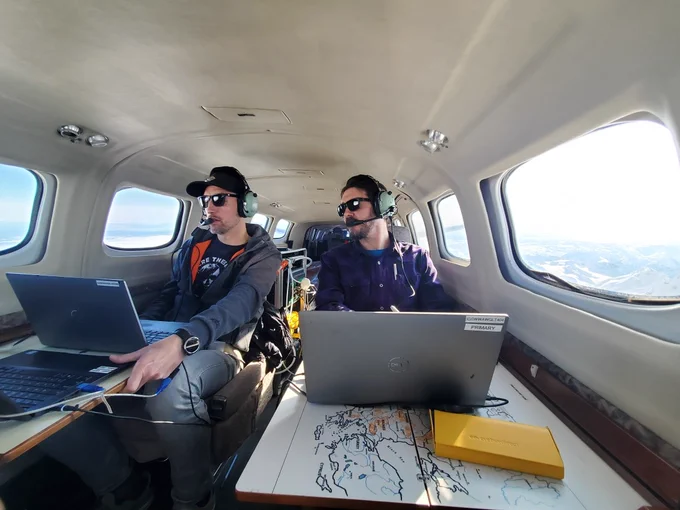 Two men sit in an airplane with maps, notebooks and laptop computers open in front of them, collecting gas emission from Mount Spurr volcano, in Alaska. Image taken March 11, 2025.