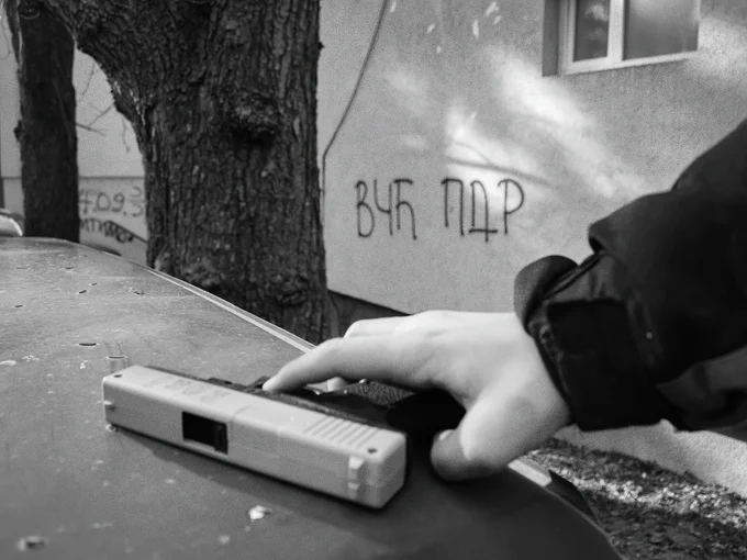  close-up shot of young hands gripping a replica rifle. The raw, symbolic image speaks of a childhood overshadowed by the past.