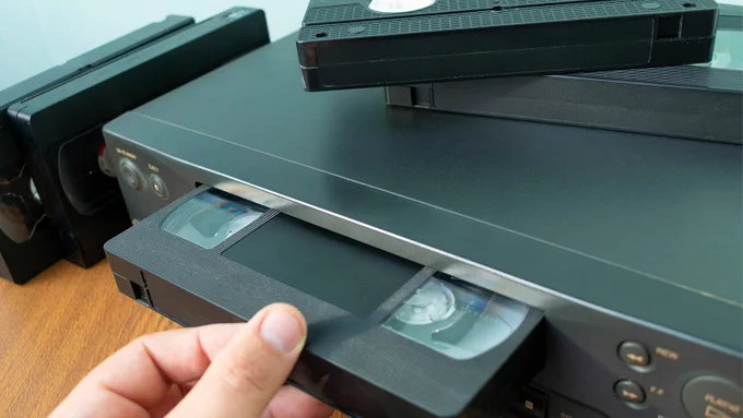 VHS videocassette is put into the video recorder to watch the video, another video cassette is on the video-tape recorder
