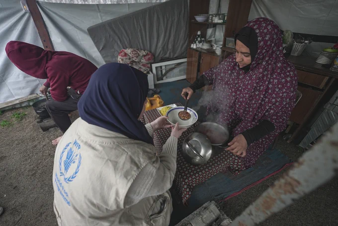 A WFP staff member helps a woman in Gaza serve food in February 2025. Since 2 March, people in Gaza have not received food aid. Commercial food prices are surging, and the situation is dire. Photo: WFP/Jaber Badwan