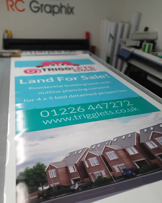 Printed graphics for a sign promoting some land for sale.  The top of the sign features the 'Trigglets Estates' logo, a pink pig peering over a white cloud, below this it has details of the site.  At the bottom is a visualisation of the 4 bed detached properties.