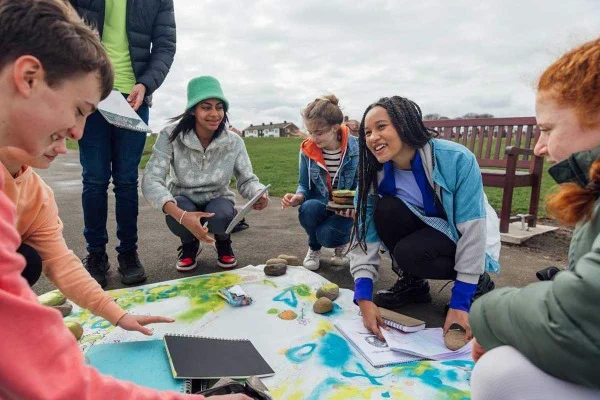 Group of teens gathered around colorful artwork on the ground outdoors.