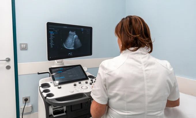 Rear view of female diagnostic sonographer conducting a liver ultrasound on a patient.