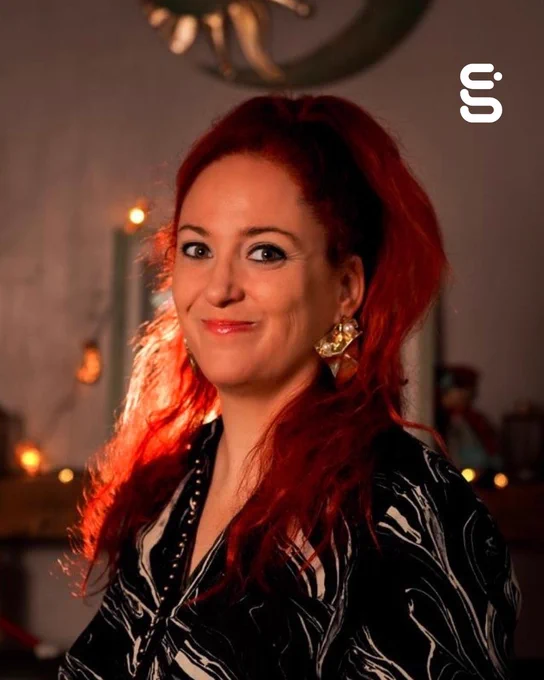 A person with red hair and a wide smile looks at the camera.
