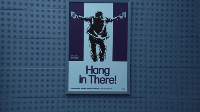 From Severance. A sign depicting a cartoon of Dylan G. flipping two switches on either side of him above the words "Hang in There!" is on a plain wall.
