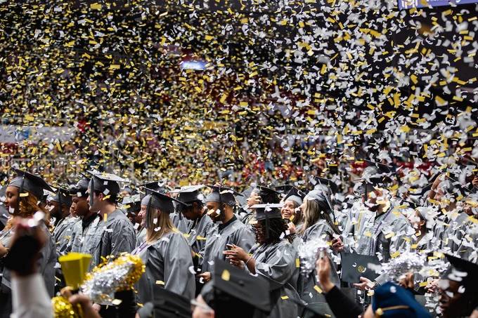 Graduates in caps and gowns celebrating under a shower of confetti.