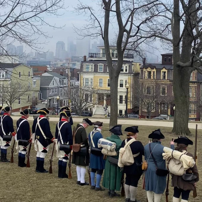 Colonial militia reenactors stand in a line at Bunker Hill, overlooking the city of Boston. 
