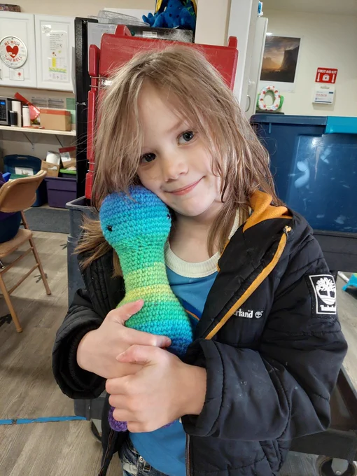 Winston UCAN Head Start student hugging a crochet dinosaur and smiling.