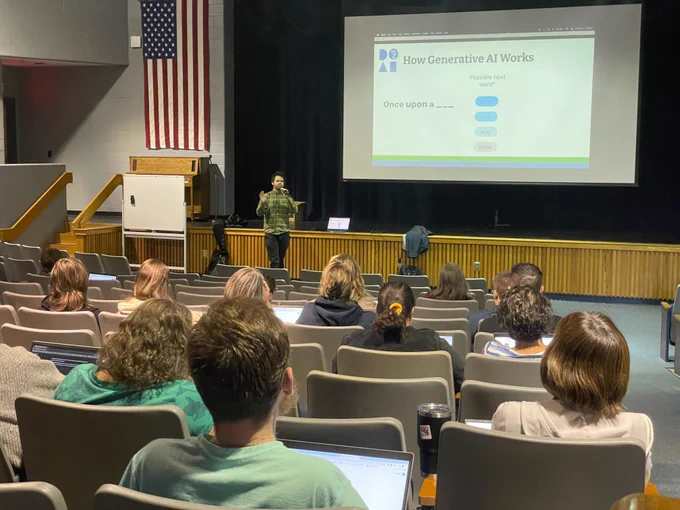 An auditorium full of teachers watching Day of AI PD trainer Matthew Taylor present on How Generative AI works