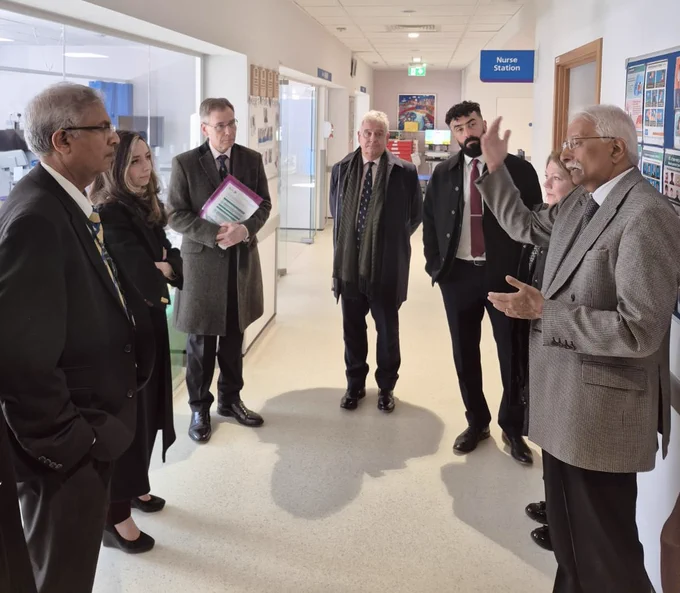 A group of people in a hospital corridor listen to a man speak