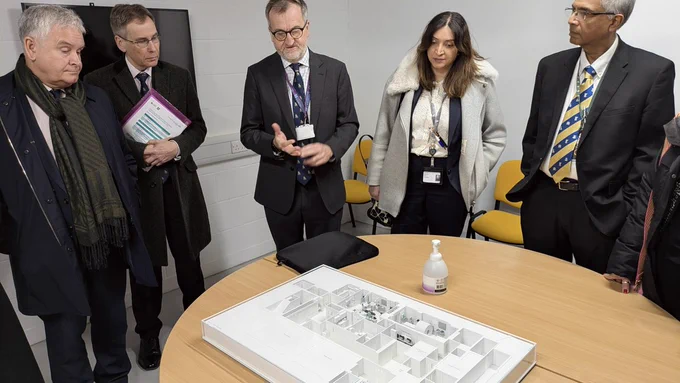 A group of people stand around a table looking at a building model