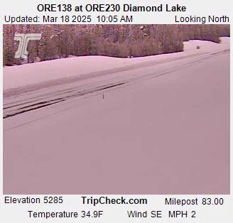 Image taken from ORE138 at ORE230 near Diamond Lake, showing a snow-covered road on March 18, 2025. The view is looking north with a temperature of 34.9°F and a wind speed of 2 MPH from the southeast.