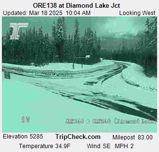 Traffic camera image of ORE138 at Diamond Lake Junction showing a snowy road and surrounding trees, with current weather information displayed including temperature and wind speed.