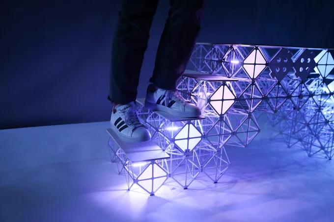 A person stands on stairs made of square voxels, lit by blue and purple light.