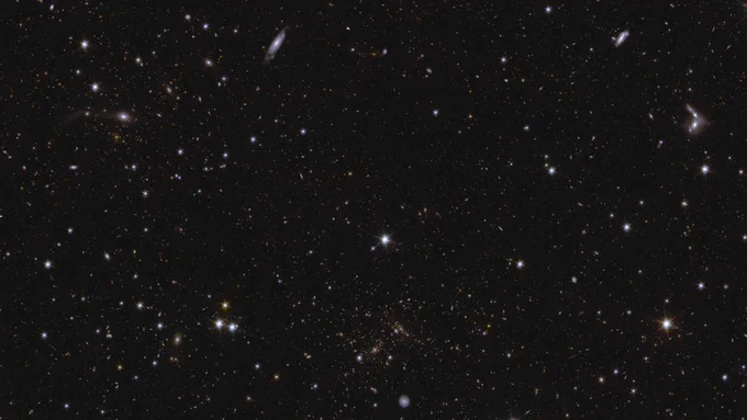 A sea of stars and galaxies sparkle against a black background. Several galaxies can be identified by their elongated shape and/or spiral arms. Some galaxies are seen edge-on while one prominent spiral galaxy at the bottom centre is seen face-on. At the far right, between the middle and top of the image, are some interacting galaxies. Galaxy clusters are also seen, in particular near bottom centre, where features smeared into arcs represent gravitational lensing. The brightest stars in the image have diffraction spikes.