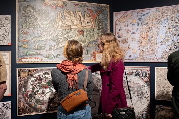 Photo © Jessie James. Photograph of two women with their backs to the camera looking at maps in a gallery.