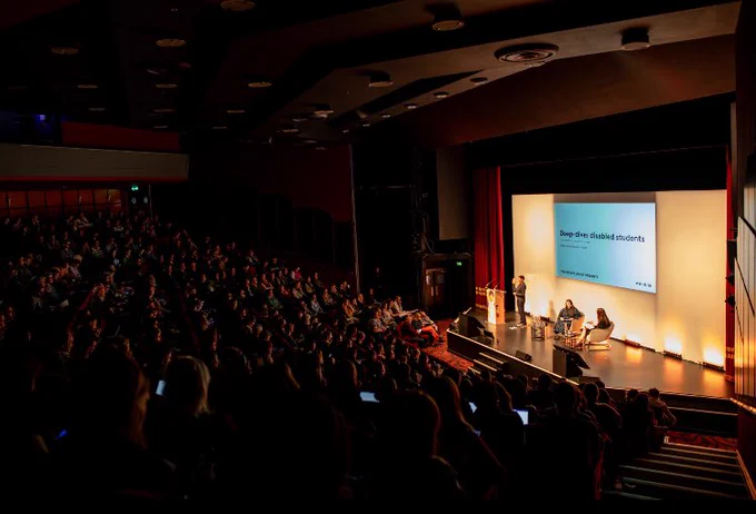 Large auditorium with two people sitting on stage, and a BSL Interpreted standing next to them. Screen behind them reads ‘Deep Dive: Disabled Students’

Photo Credit: Michael Barrow