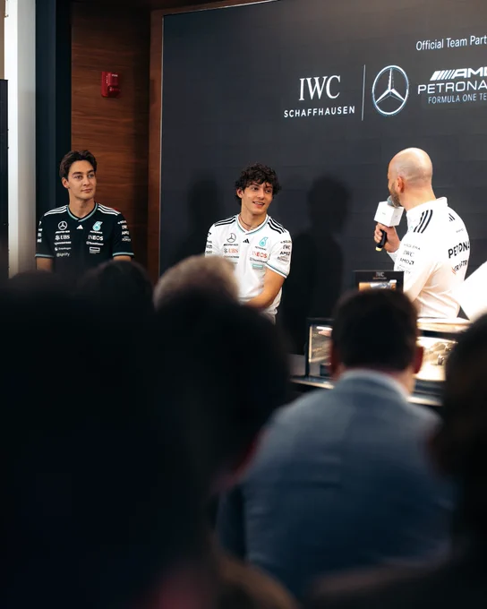 George Russell and Kimi Antonelli sit in front of a crowd whilst answering questions asked by a host beside them.