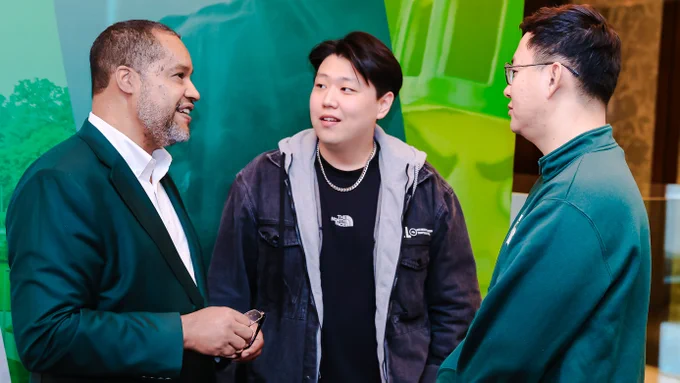 Three men speaking to one another with green backdrop behind