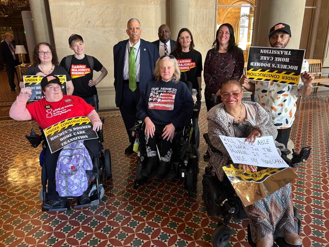 crowd of caring majority leaders with signs that read "under construction: Hochul's doomed home care transition" 