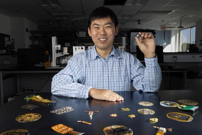Wubin Bai holds small medical devices created in his lab. There are about a dozen on the table in front of him, each roughly the size of a pill bottle or smaller.