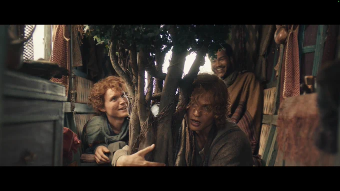 Three men around a small tree. Two in the background are smiling and laughing. One of them is hugging the small tree. There is a globe in the trunk of the tree.