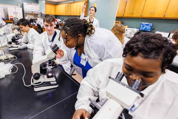 Students viewing slides through a microscope in a classroom laboratory.