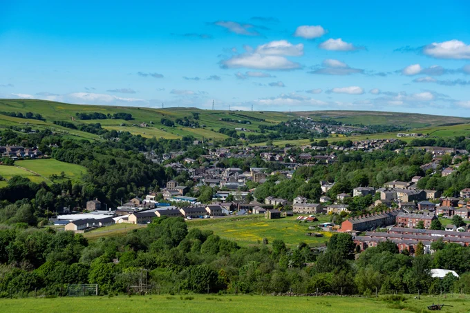Aerial view of Bacup town centre, Rossendale, surrounded by green hills and countryside under a clear blue sky