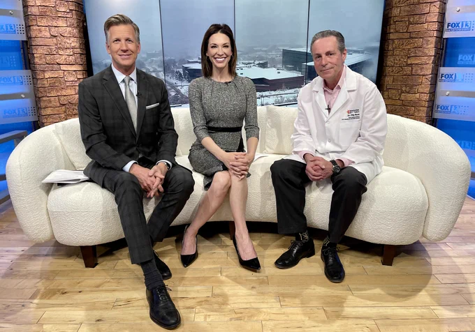 FOX13 Good Day Utah anchors, Dan Evans and Kelly Chapman, sit next to MountainStar Healthcare Chief Medical Officer, Dr. Filip Roos, on set, smiling.