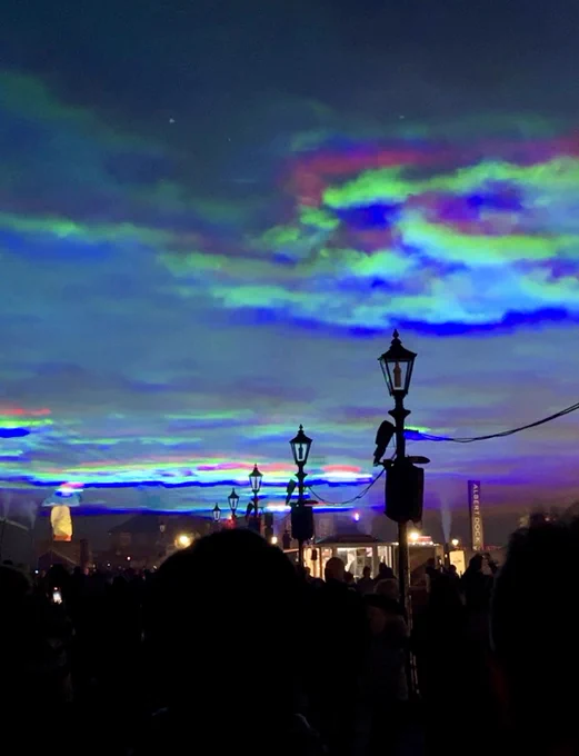 A large-scale light installation above the Royal Albert Dock at night projecting blue, green and pink colours into the sky, mimicking the Northern Lights.