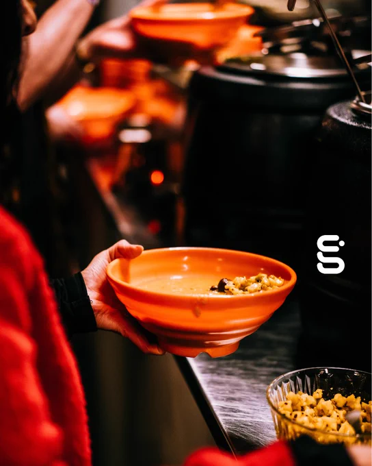 A person holds an orange bowl of daal.