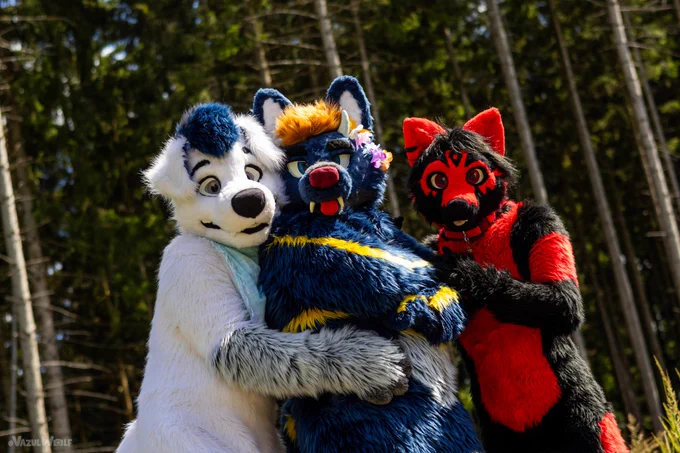 Fursuiters hugging each other in front of the forest.