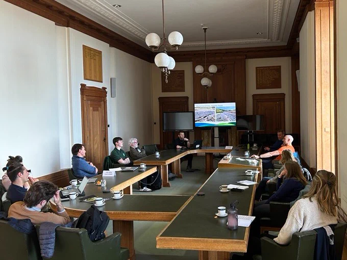 Colleagues sat around a table watching a presentation on a screen at the front of the room about the Welsh metal mines project