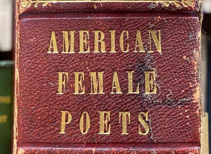 Photo of red spine of book with gold lettering “American Female Poets.”
