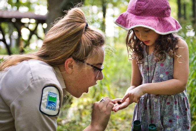 Discovery staff showing a small object to a child in a wooded area. 