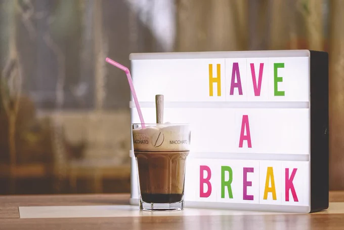 A tempting macchiato alongside a lightbox sign reading 'Have a Break', set in a cozy indoor space.