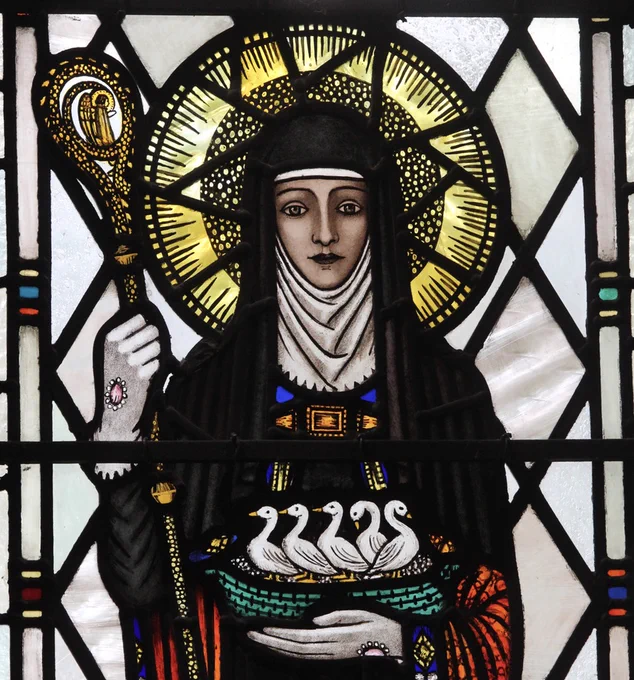 One of Trena Cox' s beautiful stained glass pieces featuring St. Werburgh with a stunning bright halo and a green woven basket of five geese in her arms which portrays her miracle of bringing a dead goose back to life.