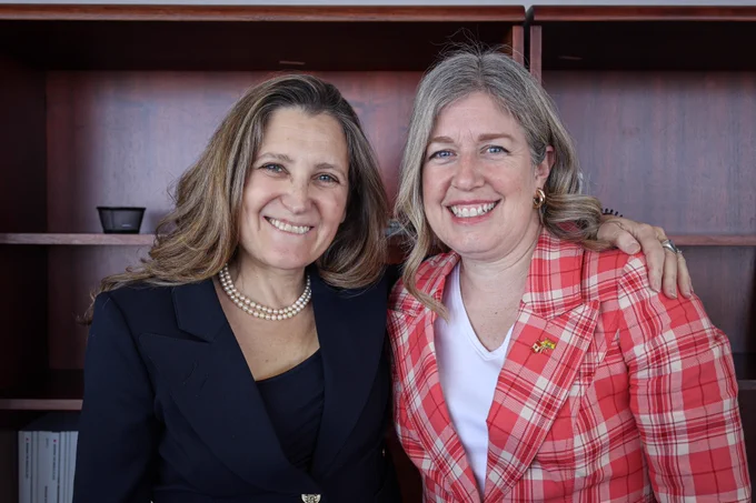 Premier Holt and internal trade minister Chrystia Freeland smiling and standing close together in front of a wooden shelf. One is wearing a black blazer and pearl necklace, and the other is in a red plaid blazer with a pin. They appear to be in a formal setting.
--
Première ministre Holt et la ministre du Commerce intérieur, Chrystia Freeland sourient et se tiennent côte à côte devant une étagère en bois. Celle de gauche porte un blazer noir et un collier de perles, et celle de droite une veste à carreaux rouges. Toutes deux paraissent heureuses et détendues.