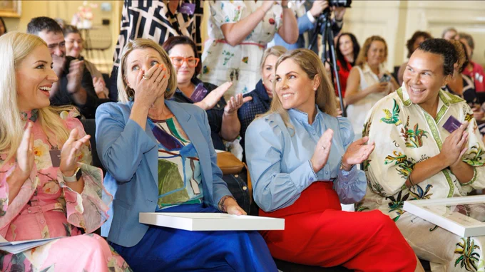 Audience members smiling and clapping at an event, with some individuals expressing surprise and delight.
