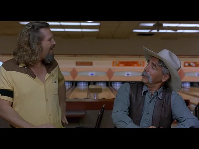We realise that the Stranger, identically dressed as before in a blue denim shirt, leather vest and cowboy hat, is seated next to the Dude at the bar. The Dude looks genuinely pleased to make the man's acquaintance again.