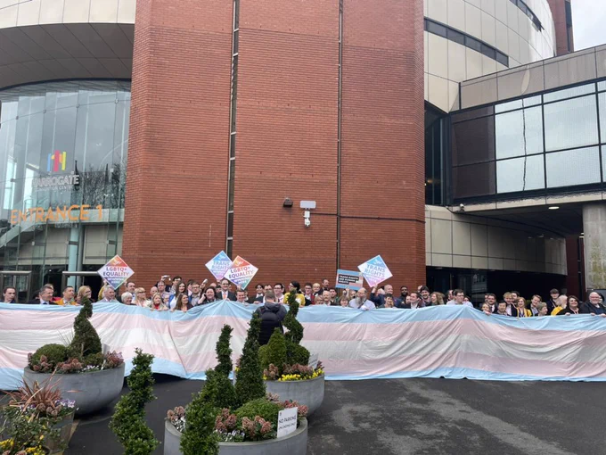 A big trans flag with many people behind it