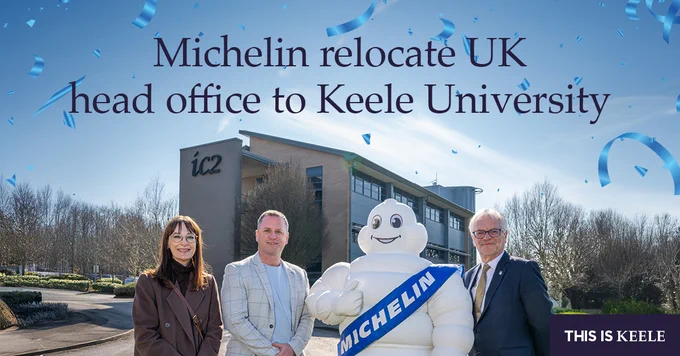 Michelin relocates UK head office to Keele University, featuring the Michelin Man mascot with three individuals in front of the university's IC2 building under a clear blue sky.