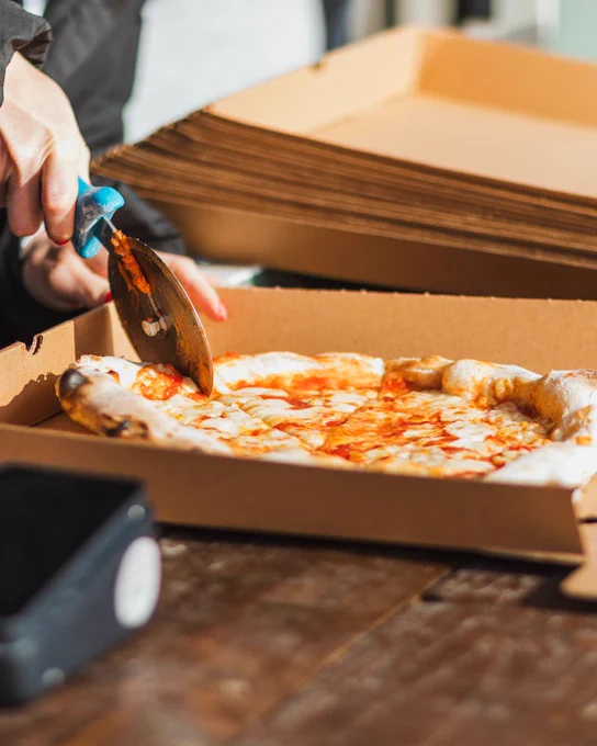 A freshly cooked pizza being cut and boxed up at a food festival