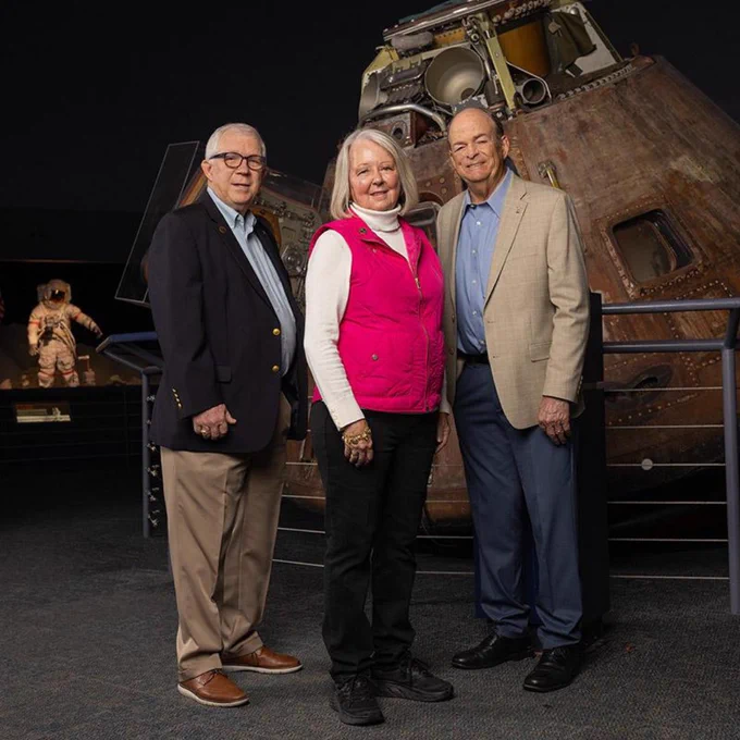 Three individuals standing in front of the Apollo command module at a museum exhibit.