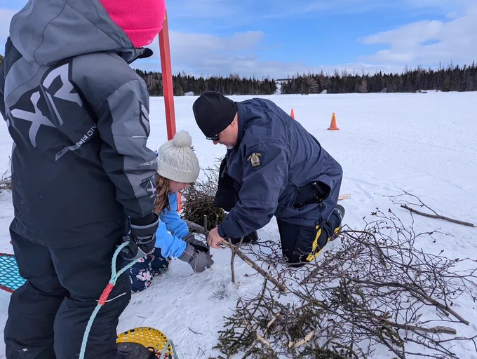 A uniformed police officer helping two students with their outdoor skills.