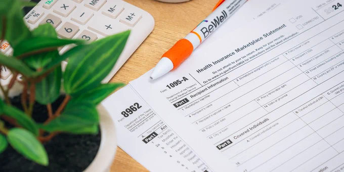 Tax forms lying on a desk next to a BeWell pen and a potted plant