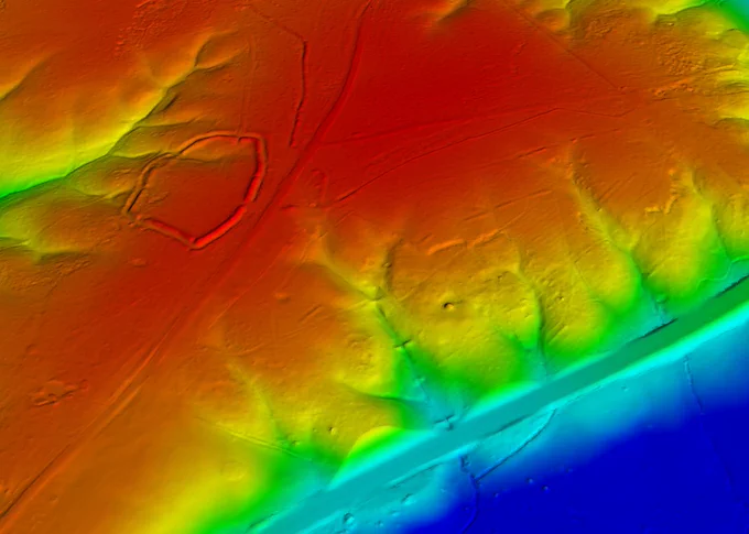 Colour extract from a Lidar digital terrain model. A rainbow colour ramp shows high ground to top left in red, sloping down through yellow and green to blue low ground at bottom right. The earthwork ramparts of Amesbury Banks Hillfort can be seen on the high ground. The line of the M25 cuts across the bottom right corner from right to left.