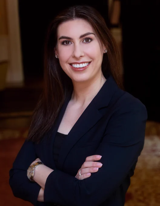 Portrait of a person wearing a dark blazer, smiling in an indoor setting.