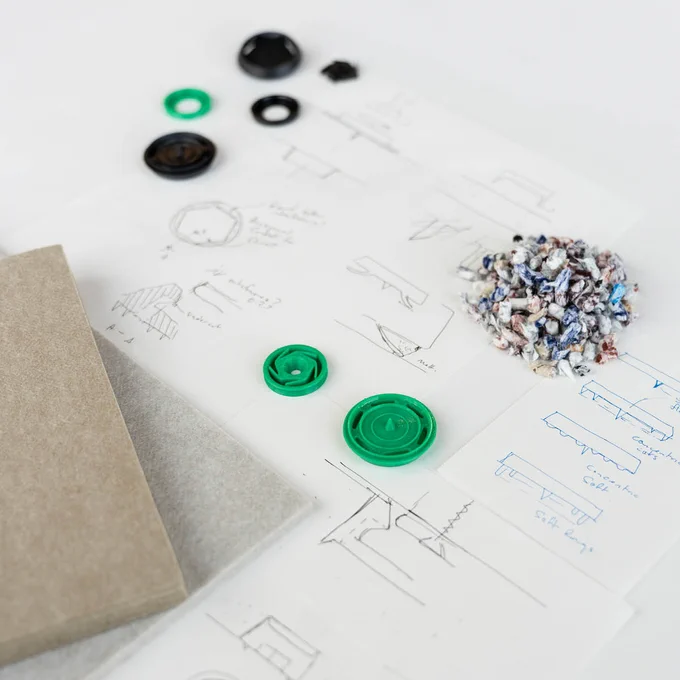 An assortment of design materials and sketches on a white surface, featuring buttons, fabric swatches, and technical drawings of chairs and tables.